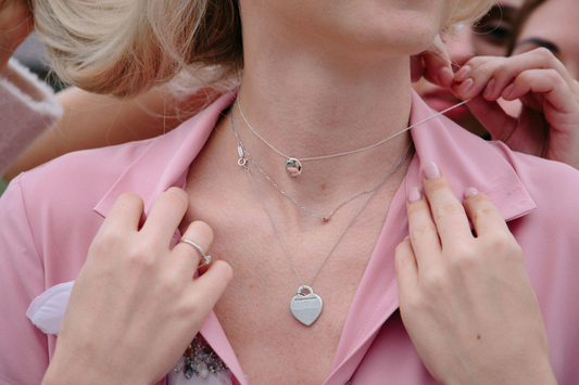 Layered silver necklaces worn over a pink blazer