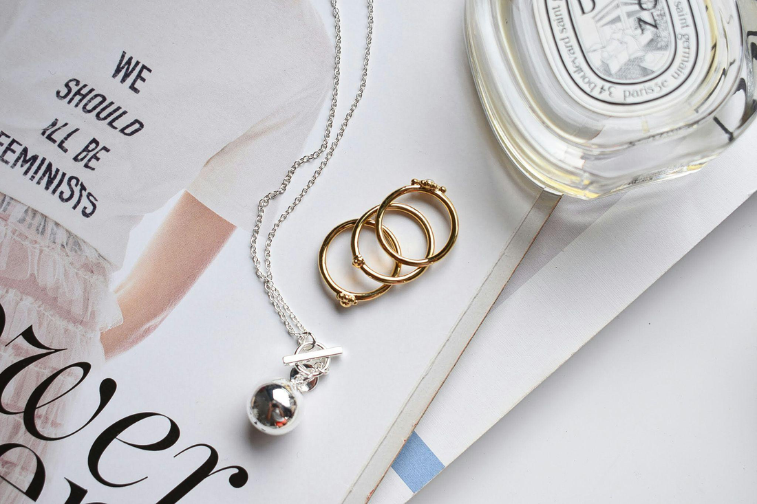 gold rings and a silver necklace on a magazine page beside a perfume bottle