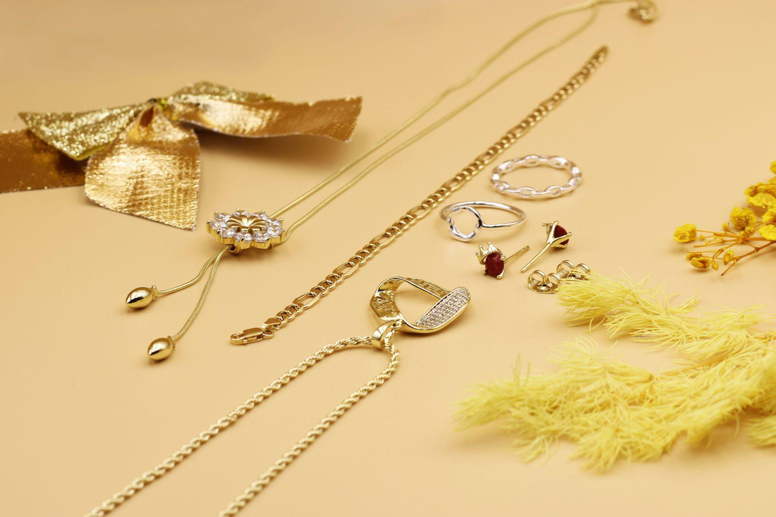 gold necklaces, rings, and earrings arranged on a warm beige surface