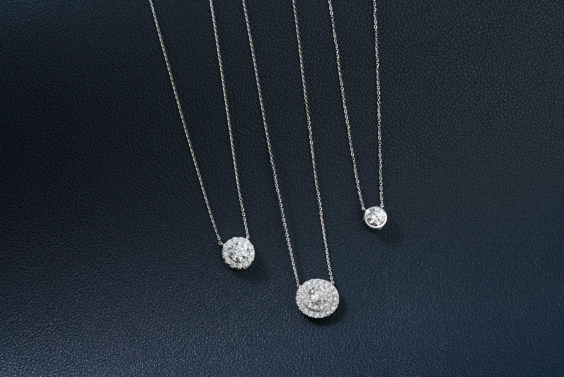three diamond pendant necklaces on a dark surface