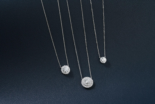 three diamond pendant necklaces on a dark surface